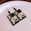 Detalle de pendientes rectangulares negros con incrustación de cara sobre plato blanco - Estilo Retrato Abstracto de Rectángulo Negro