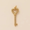 Détail d'un pendentif clé en forme de cœur doré orné de strass brillants sur fond beige - Pendentif Clé de Cœur Zircon - Or - Diamant Blanc