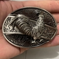 Detailliertes Hahn-Relief auf einer ovalen Gürtelschnalle aus Altsilber in der Hand - Hahn