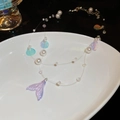 Detailed macro of iridescent mermaid tail pendant and pearls on a ceramic tray - Iridescent Purple White