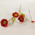 Vibrant red faux poppy flower stem with blooming petals and buds on a book background - Red