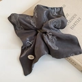 Detailed macro view of dark grey paisley silk hair scrunchie with oval metal brand tag - Wrinkled / Gray