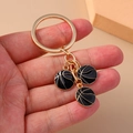 Close-up of golden metal keychain with three black enamel basketball pendants on a plain surface - Black