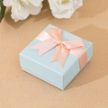 Light blue square jewelry gift box with a pink ribbon bow and paperboard texture - Blue Box Pink Bow