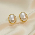 Macro shot of oval pearl earrings with gold frames on smooth beige silk fabric - Pearl Earrings