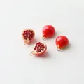 Detailed macro view of four resin pomegranate charms with gold loops for DIY jewelry - Half Pomegranate