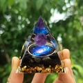 Orgone pyramid with amethyst sphere and blue galaxy pattern held against green background - Style 18