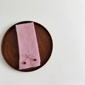 Detalle de calentador de punto rosa con un lazo fino y pompones de color marrón rojizo - Rosa