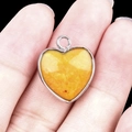 Silver-edged heart pendant with yellow stone inlay held against a dark background - Yellow Jade Silver Edging
