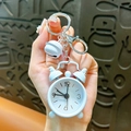 Miniature light blue alarm clock keychain with bell pendant, shown held in hand. - White