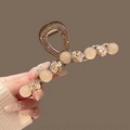 Elegant gold metal hair claw with cream pearls and rhinestones shown in hand - Camellia One-Line Claw 11cm