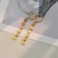 Detailopname van gouden hangende oorbellen met schelpvormige pailletten op stijlvolle achtergrond - Schelpmateriaal / Goud