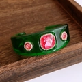 Makroaufnahme einer grünen Harz-Manschette mit rosa Kristallen und Diamantenbesatz - Grüner Armreif Mit Rosenrotem Stein