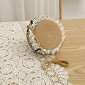 Close-up of woven straw round bag with white ruffled edges and black bow details - Circular Straw Bag / Bag-Khaki