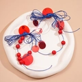 Close-up of ethnic blue cord earrings featuring red sequins and beads on a ceramic plate - Red