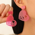 Pink glitter acrylic heart earrings with LOVE engraving shown on model's ear - Sequin Love Pink Heart (WG-1432)