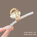 Detail of 11cm gold metal hair claw with pearls and heart charms on a brown background - K18 Double Hearts