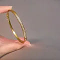 Close-up of gold titanium bangle with single row pavé zircon and side buckle clasp - Gold Color (A-10)