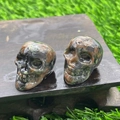Polished green and brown natural stone mini crystal skulls on a dark wood block - Sesame Stone