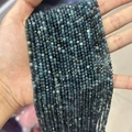Strands of faceted blue-green natural gemstone beads shown in a hand-held display - Blue Tourmaline 3mm