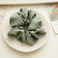 Detail of sage green satin scrunchie with metallic tag and silky smooth texture - Green