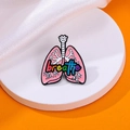 Pink enamel lung brooch with rainbow breathe text on a white pedestal display - Rainbow Breathe Lung (C2542-2)