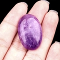 Oval purple crystal gemstone for DIY jewelry settings held in hand with black background - Amethyst
