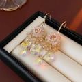 Détail de boucles d'oreilles bohèmes avec cristaux de zircon et glands floraux dans l'écrin - Style Crochet Or-Rose