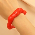 Nahaufnahme eines glänzenden roten Harzarmreifens mit wellenförmigem Design am Handgelenk - Unregelmäßig Höckerig (21) / Rot