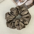 Detail of dark brown satin scrunchie with soft pleats on a textured background - Brown