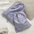 Detail view of two purple drawstring storage bags in different sizes on white bedding - Small (30x37cm) / Light Purple