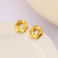 Vista macro di orecchini a cerchio esagonali dorati su un piatto di ceramica bianca - Oro