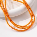 Collana multifilo di piccole perline arancioni disposta a strati su un supporto bianco - 1 Pezzo / Arancione