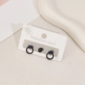 Detailed macro view of minimalist black stainless steel stud earrings set on a display card - Round Style / Black