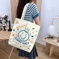 Beige canvas shoulder bag with colorful cartoon pig print worn by a model in a cozy home setting - Happy Face