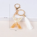 Detailed view of resin letter X keychain with gold foil, white shell fragments and silk tassel - Letter X