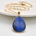 Detailed shot of a gold teardrop lapis lazuli pendant resting on a white ceramic plate - Flat Teardrop