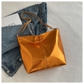 Detail of a shiny metallic orange bucket bag with golden chain strap on denim fabric - Orange
