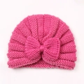 Detail of rose pink baby knitted hat featuring a large textured bow on a flat surface - Rose Red