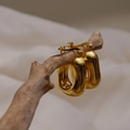Detail von goldenen U-förmigen Creolen an einem Ast mit natürlicher Holzmaserung-Szene - Gold