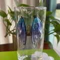 Detailed macro view of gradient cicada wing earrings hanging on a glass rim with sparkles - Blue Silver Foil
