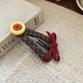 Nahaufnahme der braunen Karo-Haarspange mit gelbem Knopf und roter Schleife - Rot-Gelbe Knopf Schnabelspange