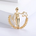 Detailed close-up of a golden Lady Justice brooch featuring scales and an olive branch - Polished Gold