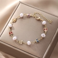 Detalle de una pulsera de mariposa dorada con perlas blancas y dijes de colores - Pulsera de perlas redondas de mariposa