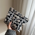 Dettaglio della pochette in maglia nera con motivi a onde trapuntati bianchi e logo simple wish - Ricamo Anemone 3D