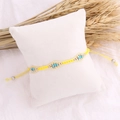 Detail of yellow woven seed bead bracelet with blue accents on a white display pillow - Yellow