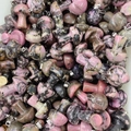 Pink rhodonite gemstone mushroom pendants with silver metal loops in bulk display - Rhodonite