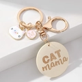 Chic CAT MAMA gold keychain with cartoon cat charm and pink M pendant on white stand - Beige