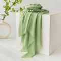 Light green cotton linen scarf with frayed edges displayed on a white minimal stand - Grass Green