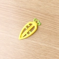Yellow carrot-shaped hair clip with green leaves on a clean wooden background - Yellow